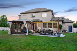 Back of property at dusk featuring a gazebo, stucco siding, a shingled roof, an outdoor hangout area, and a patio area