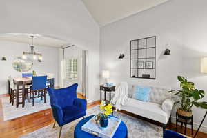 Living room with arched walkways, wood finished floors, a chandelier, and high vaulted ceiling
