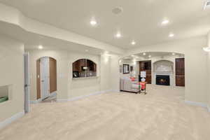 Living room with light colored carpet, recessed lighting, a warm lit fireplace, and arched walkways