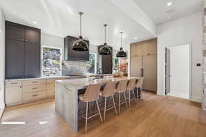 Kitchen featuring a kitchen breakfast bar, light wood finished floors, light stone counters, decorative backsplash, and decorative light fixtures