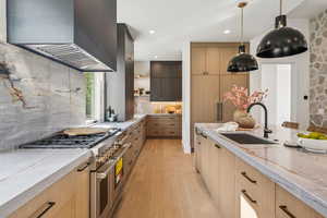 Kitchen with light stone counters, range with two ovens, open shelves, light wood-type flooring, and wall chimney range hood