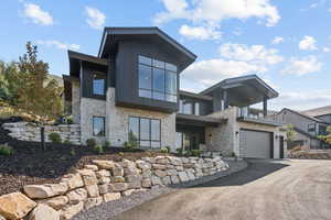 View of front facade featuring stone siding, a garage, driveway, and a balcony