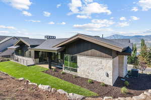 Rear view of house with stone siding, a shingled roof, and a yard