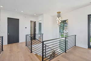 Hall with an upstairs landing, light wood-style floors, recessed lighting, and a chandelier