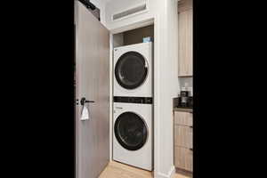 Laundry room with stacked washing machine and dryer, light wood-type flooring, and a barn door