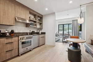 Kitchen with stainless steel appliances, dark countertops, range hood, light wood finished floors, and open shelves