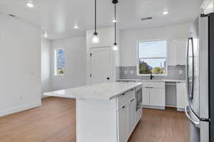Kitchen featuring stainless steel appliances, light wood-style floors, white cabinetry, pendant lighting, and a kitchen island