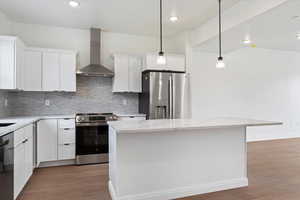 Kitchen featuring appliances with stainless steel finishes, white cabinets, wall chimney range hood, light stone countertops, and a kitchen island