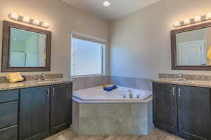 Full bath featuring two vanities, wood finished floors, a bath, and recessed lighting