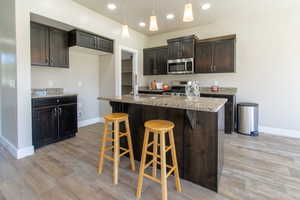 Kitchen with recessed lighting, stainless steel appliances, a kitchen bar, a kitchen island with sink, and dark brown cabinets