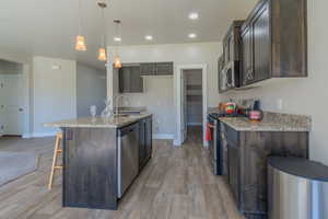 Kitchen with appliances with stainless steel finishes, light wood-type flooring, light stone countertops, dark brown cabinets, and recessed lighting