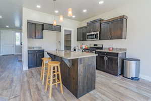 Kitchen with recessed lighting, appliances with stainless steel finishes, light wood-type flooring, light stone countertops, and hanging light fixtures