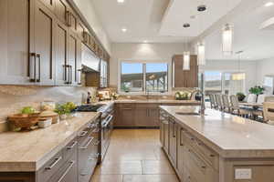 Kitchen with recessed lighting, range with two ovens, a kitchen island with sink, light stone counters, and decorative light fixtures