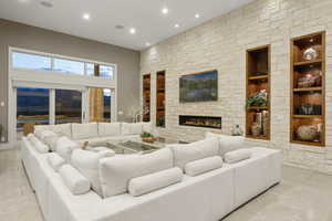 Tiled living area with built in shelves, recessed lighting, an outdoor stone fireplace, and a high ceiling