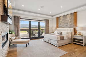 Bedroom featuring access to outside, wood finished floors, a large fireplace, a tray ceiling, and recessed lighting