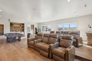 Home theater room with light wood-style floors, recessed lighting, and bar area
