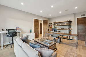 Living room with an office area, light wood-type flooring, and recessed lighting