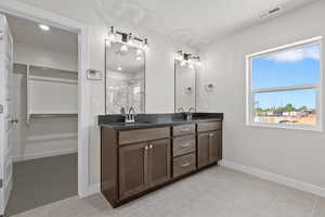 Full bathroom with double vanity, a walk in closet, a shower, and tile patterned flooring