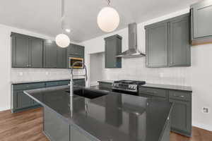 Kitchen with wall chimney range hood, stainless steel gas range oven, dark countertops, dark wood-style floors, and decorative light fixtures