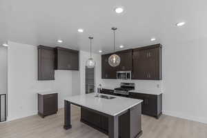 Kitchen with stainless steel appliances, dark brown cabinets, recessed lighting, light countertops, and a kitchen island with sink