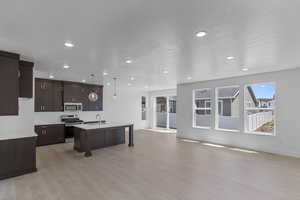 Kitchen with light countertops, stainless steel appliances, a kitchen breakfast bar, open floor plan, and a center island with sink