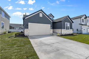 Ranch-style house featuring stone siding, stucco siding, an attached garage, and a front yard