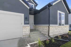 Entrance to property featuring stone siding, stucco siding, and an attached garage
