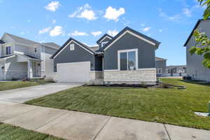 View of front facade featuring stone siding, stucco siding, an attached garage, driveway, and a front yard