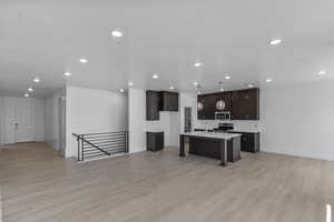 Kitchen featuring a kitchen island with sink, recessed lighting, light countertops, open floor plan, and dark brown cabinetry