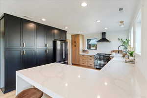 Kitchen with light stone countertops, recessed lighting, high end appliances, wall chimney exhaust hood, and a peninsula