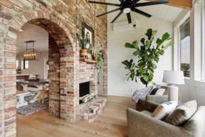 Living room featuring wood finished floors, ceiling fan, a fireplace, a wall mounted air conditioner, and arched walkways