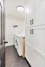 Laundry room featuring cabinet space, separate washer and dryer, and dark tile patterned floors