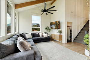 Living area featuring beamed ceiling, wood finished floors, ceiling fan, stairs, and high vaulted ceiling