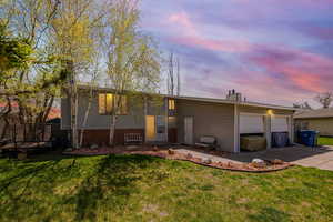 View of front of house with an attached garage, concrete driveway, and a lawn