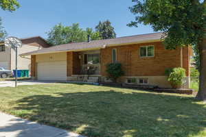 View of front facade featuring brick siding, an attached garage, a front yard, and concrete driveway