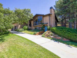 View of front of home featuring brick, a chimney, concrete driveway, a front lawn and an attached garage