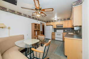 Kitchen featuring light brown cabinetry, white appliances, ceiling fan, and dark tile patterned flooring