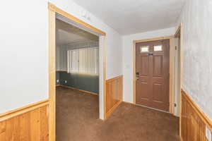 Foyer entrance featuring a wainscoted wall, wooden walls, dark colored carpet, a textured ceiling, and wallpapered walls