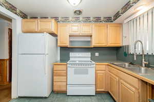 Kitchen with white appliances, light brown cabinetry, under cabinet range hood, and light tile patterned flooring