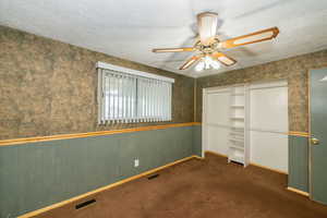 Unfurnished bedroom with a textured ceiling, wallpapered walls, carpet floors, a closet, and a ceiling fan
