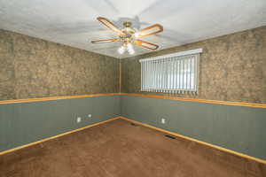 Carpeted spare room with wallpapered walls, a textured ceiling, a wainscoted wall, and a ceiling fan