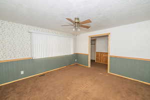 Unfurnished bedroom with a textured ceiling, wainscoting, carpet floors, wallpapered walls, and a ceiling fan