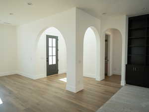 Entryway with arched walkways, light wood-type flooring, and recessed lighting