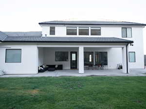 Back of house with stucco siding, outdoor lounge area, a patio, and a lawn
