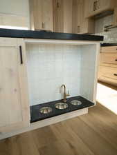 Kitchen view of tasteful backsplash, dark countertops, wood finished floors, pot filler, and light brown cabinetry