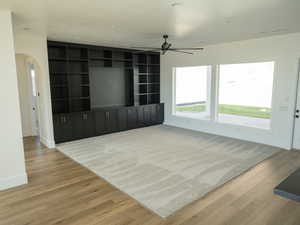 Unfurnished living room featuring light wood-style floors, arched walkways, ceiling fan, and recessed lighting