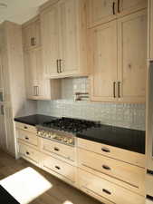 Kitchen with tasteful backsplash, dark countertops, light wood-style floors, and stainless steel gas stovetop