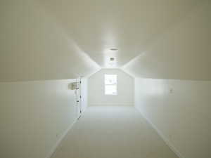Bonus room with light colored carpet and vaulted ceiling