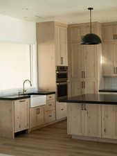 Kitchen with light brown cabinets, dark countertops, backsplash, stainless steel double oven, and wood finished floors