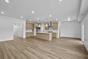 Kitchen with open floor plan, an island with sink, light wood-style floors, light countertops, and recessed lighting